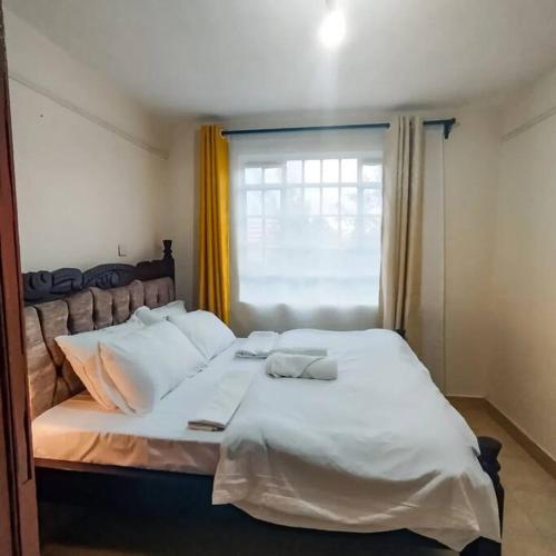 Cette chambre comprend un grand lit blanc et une fenêtre. dans l'établissement Cosy Homes Eldoret, à Eldoret