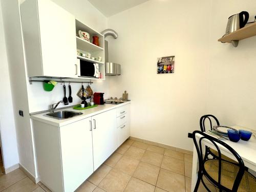 cocina con armarios blancos, fregadero y mesa en Rosa's House - zona ospedaliera, en Cagliari