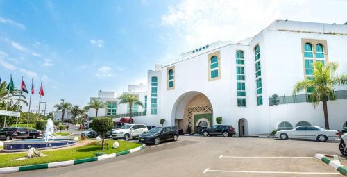 un grand bâtiment blanc avec des voitures garées dans un parking dans l'établissement Hotel Rabat - A member of Barceló Hotel Group, à Rabat