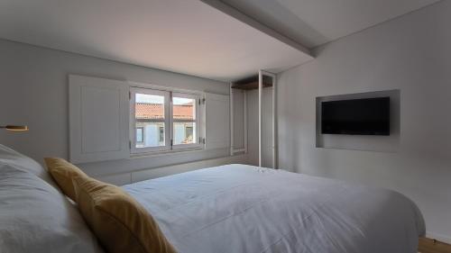 a white bedroom with a bed and a television at DOMI Suites & Studios in Guimarães