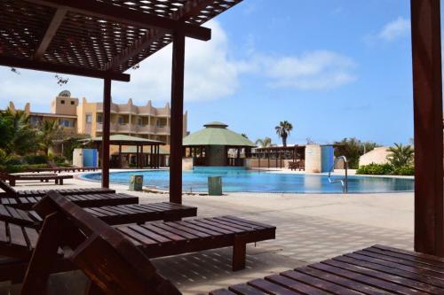 - une piscine avec bancs en bois en face d'un complexe dans l'établissement Tropical Morabeza Apartment Santa Maria, à Santa Maria