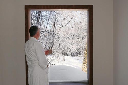 un homme en blanc tenant une tasse donnant sur une fenêtre dans l'établissement Blue Hill Pool spa game room mountain view, à Morin Heights