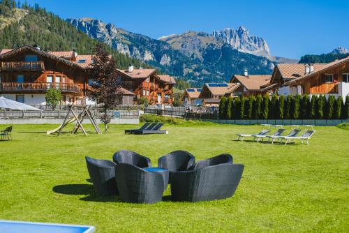 een groep stoelen in een veld met bergen bij Hotel Arnika in Pozza di Fassa