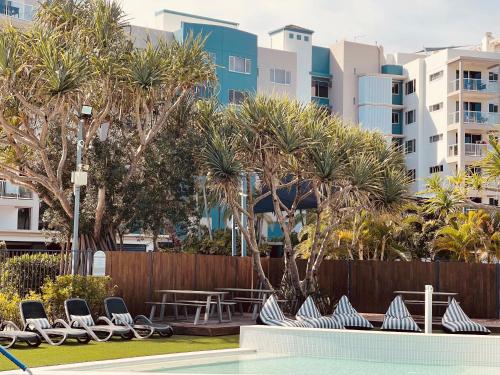 a swimming pool with chairs and trees and buildings at Atlantis Marcoola in Marcoola