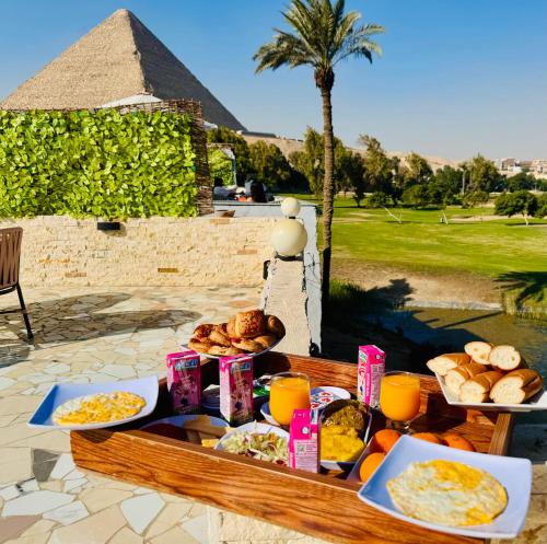 einen Tisch mit Frühstückslebensmitteln und eine Pyramide im Hintergrund in der Unterkunft Golf Pyramids View in Kairo