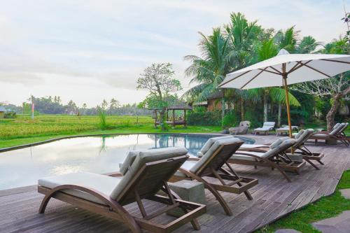 eine Gruppe Stühle und ein Sonnenschirm neben einem Pool in der Unterkunft Arya Villas Ubud in Ubud