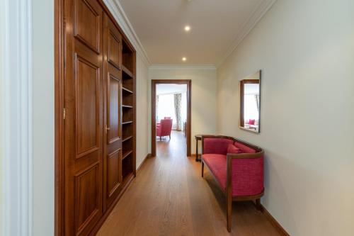 un couloir avec une chaise rouge et une porte en bois dans l'établissement Suvretta House, à Saint-Moritz