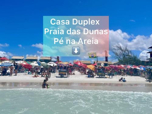 a beach with people and umbrellas and a sign at Casa Duplex Praia Das Dunas - Pé na Areia - Ar Condicionado - Alto Padrão in Cabo Frio