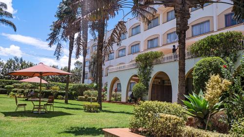 un hôtel avec une table, des chaises et des palmiers dans l'établissement Sirikwa Hotel, à Eldoret