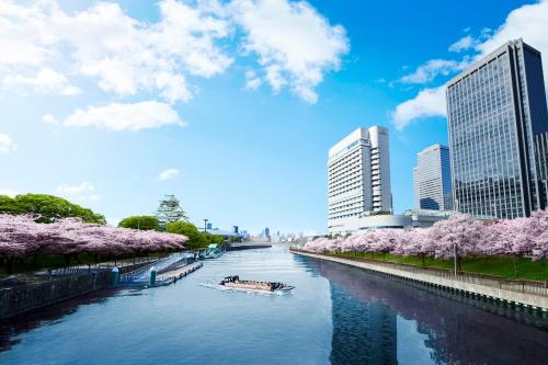 un barco en un río en una ciudad con cerezos en Hotel New Otani Osaka, en Osaka