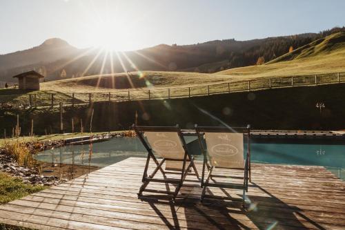 une chaise assise sur une promenade en bois à côté d'un étang dans l'établissement Hotel Lammwirt, à Grossarl