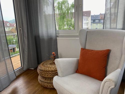 een witte stoel met een oranje kussen in een kamer met een raam bij discovAIR Eisenach - 3-Zi-Apartment Jakob- Schwimmbad-Nah mit Netflix in Eisenach