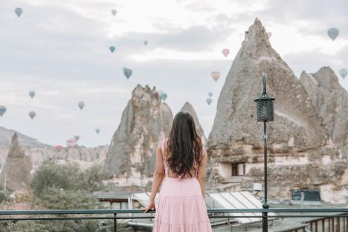 Uma mulher de vestido rosa a olhar para balões de ar quente. em Turan Cappadocia Cave em Goreme