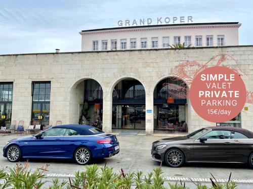 two cars parked in a parking lot in front of a building at Hotel Grand Koper in Koper