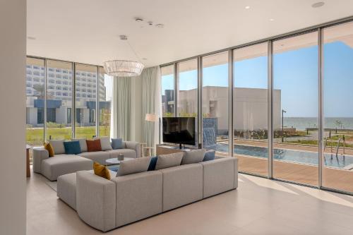 ein Wohnzimmer mit 2 Sofas, einem TV und großen Fenstern in der Unterkunft Ajman Hotel by Blazon Hotels in Ajman 