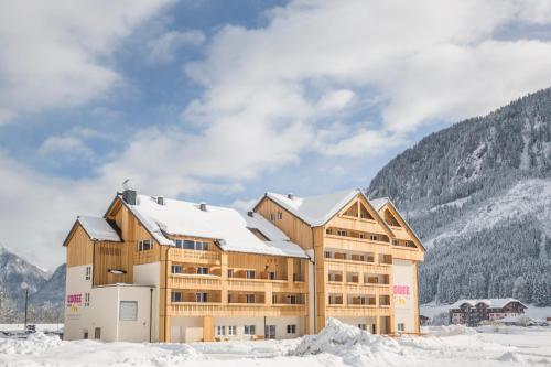 ein Gebäude im Schnee mit Bergen im Hintergrund in der Unterkunft COOEE alpin Hotel Dachstein in Gosau