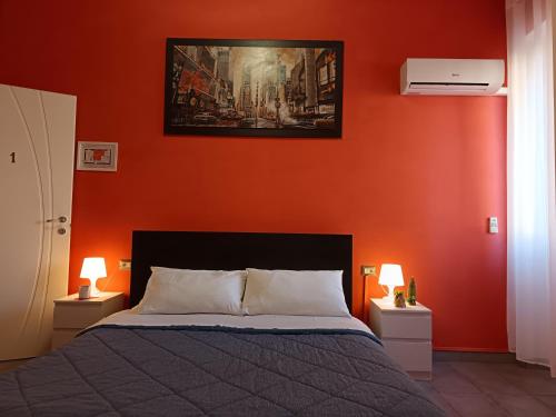 a bedroom with an orange wall with a bed and two lamps at Adriatic Room 50 m dalla stazione Ferroviaria di Ciampino e dalla navetta aeroportuale in Ciampino