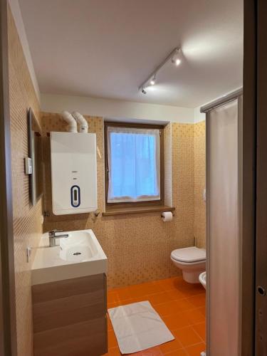 a bathroom with a sink and a toilet and a window at Appartamenti Home Service in Arabba