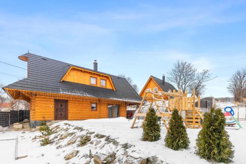 uma cabana de madeira na neve com um parque infantil em Kukana & Kuku em Vysoké Tatry