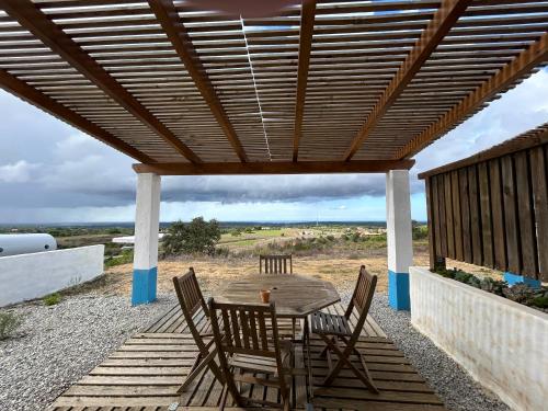 uma mesa de madeira e cadeiras sob uma pérgola de madeira em Monte Sardinha em Santiago do Cacém