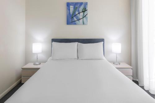 una camera da letto con un grande letto bianco con due lampade di Park Regis City Quays a Cairns