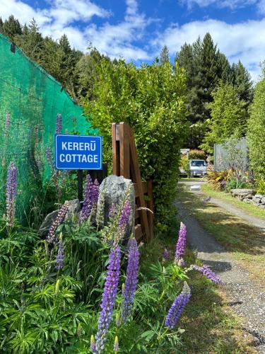 Kereru Cottage, Cosy Log Cabin, Serene Lake & Mountain Views في كوينزتاون: علامة في حديقة مع الزهور الأرجوانية