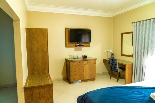 Schlafzimmer mit einem Bett, einem Schreibtisch und einem TV in der Unterkunft Windhoek Gardens Boutique Hotel in Windhoek