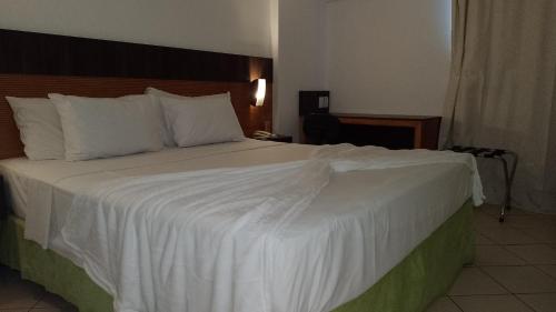 a bedroom with a large bed with white sheets and pillows at Natal Plaza Suítes- Ponta Negra in Natal