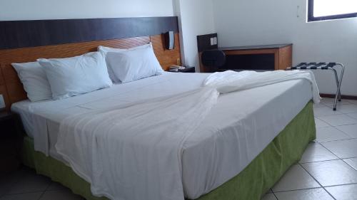 a bedroom with a large bed with white sheets and pillows at Natal Plaza Suítes- Ponta Negra in Natal