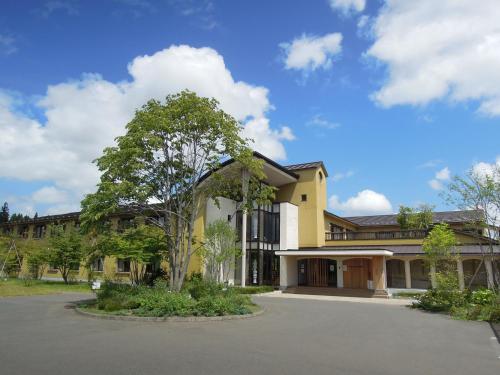 un bâtiment jaune avec un arbre dans un parking dans l'établissement Hotel Folkloro Hanamakitowa, à Hanamaki