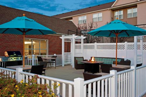 Residence Inn Lansing West في Delta Center Township: فناء به طاولات ومظلات على سياج