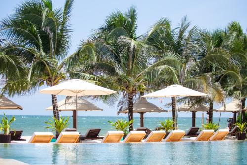 una piscina con sedie, ombrelloni e oceano di Mana Mui Ne Beach Resort & Spa a Mui Ne