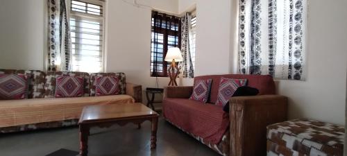 ein Wohnzimmer mit Sofas, einem Tisch und Fenstern in der Unterkunft Madhav Bhavan Guest House in Pune