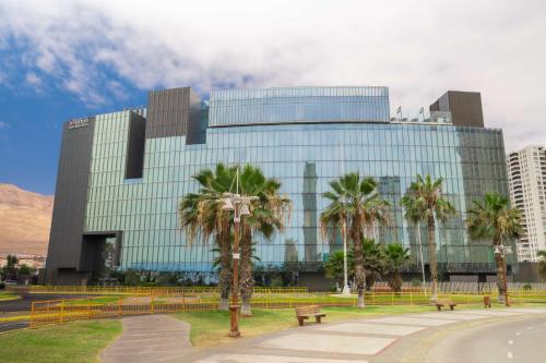 a glass building with palm trees in front of it at Hilton Garden Inn Iquique in Iquique