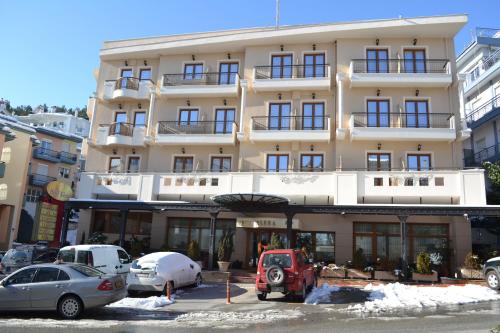 een groot wit gebouw met auto's geparkeerd voor het bij Elena Hotel in Kozani