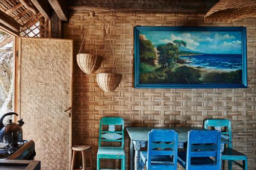 una sala da pranzo con sedie blu e un dipinto sul muro di The Island Houses Bingin a Uluwatu