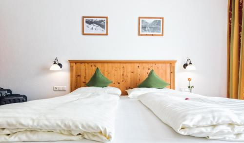 two beds in a bedroom with white sheets and green pillows at Apparthotel AlpenChalet in Neukirchen am Großvenediger