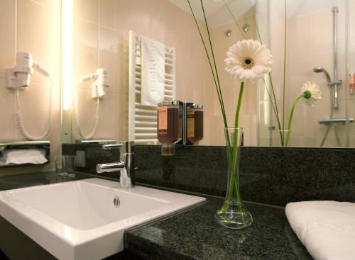 a bathroom with a sink and a vase with a flower in it at IntercityHotel Mainz in Mainz