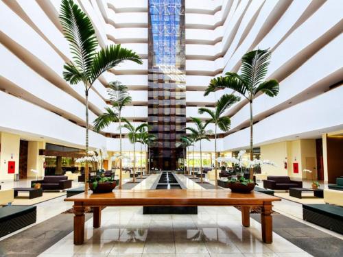 un grand hall avec une table et des palmiers dans l'établissement Apartamento Suites Le Jardin Caldas Novas Goiás, à Caldas Novas