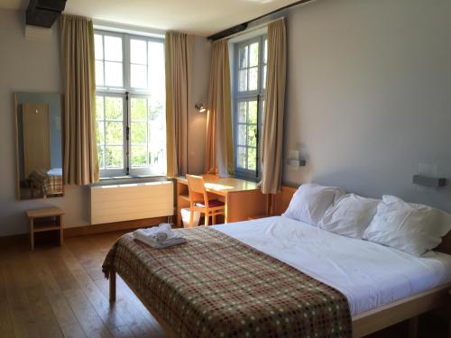 - une chambre avec un lit, un bureau et des fenêtres dans l'établissement Irish College Leuven, à Louvain