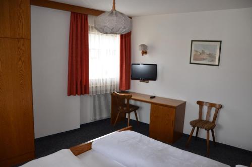 ein Hotelzimmer mit einem Bett, einem Schreibtisch und einem TV in der Unterkunft Gasthof Toni in Kastelruth