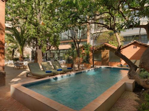 einen Pool im Innenhof mit Stühlen und Bäumen in der Unterkunft H10 Casa Mimosa 4* Sup in Barcelona