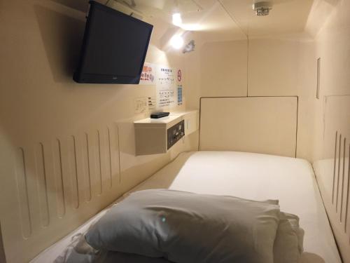 um pequeno quarto com uma cama e uma televisão de ecrã plano em Capsule&Spa Grand Sauna Hiroshima (Male Only) em Hiroshima