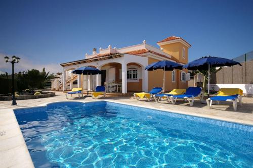 a pool with chairs and umbrellas in front of a house at Vv Tirma in Caleta De Fuste