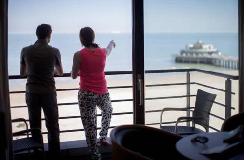 zwei Menschen, die aus einem Fenster auf den Ozean blicken in der Unterkunft Hotel Riant-Séjour by WP Hotels in Blankenberge