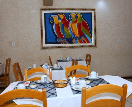 een tafel met stoelen en een schilderij van papegaaien bij Pousada Águas do Forte in Cabo Frio