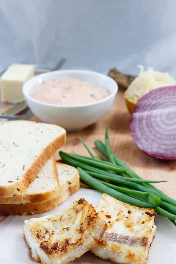 Fillets of cod, slices of bread, bowl of salad dressing, and cut onions.