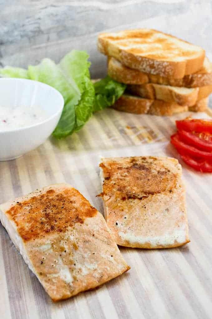 Assembling a salmon sandwich: Seared Pink Salmon, Sliced Tomatoes, Toasted Bread, Lettuce, and Dijon Sauce. Sandwich Ingredients before Sandwich is Assembled.