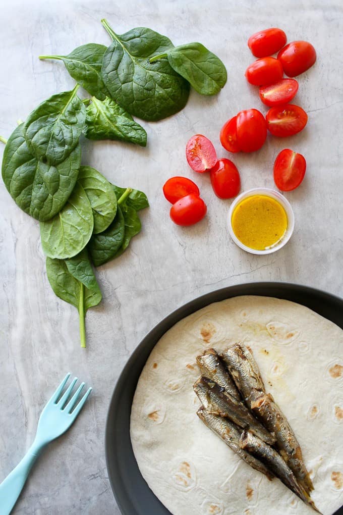 Fish wraps with sardines, tomatoes, dressing, and spinach on a countertop