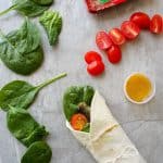 Fish wraps with sardines, tomatoes, dressing, and spinach on a countertop